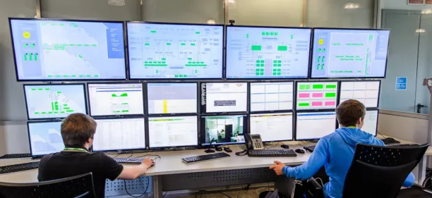 Picture of 2 male analysts sitting behind multiple screens monitoring unknown processes in real-time. 